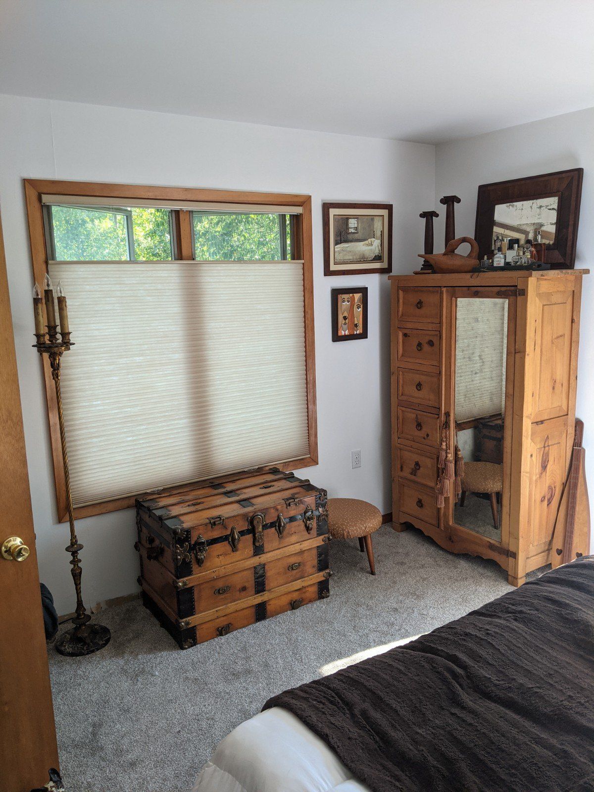 Bedroom with a wooden wardrobe, chest, and window with a view. Gray carpet.