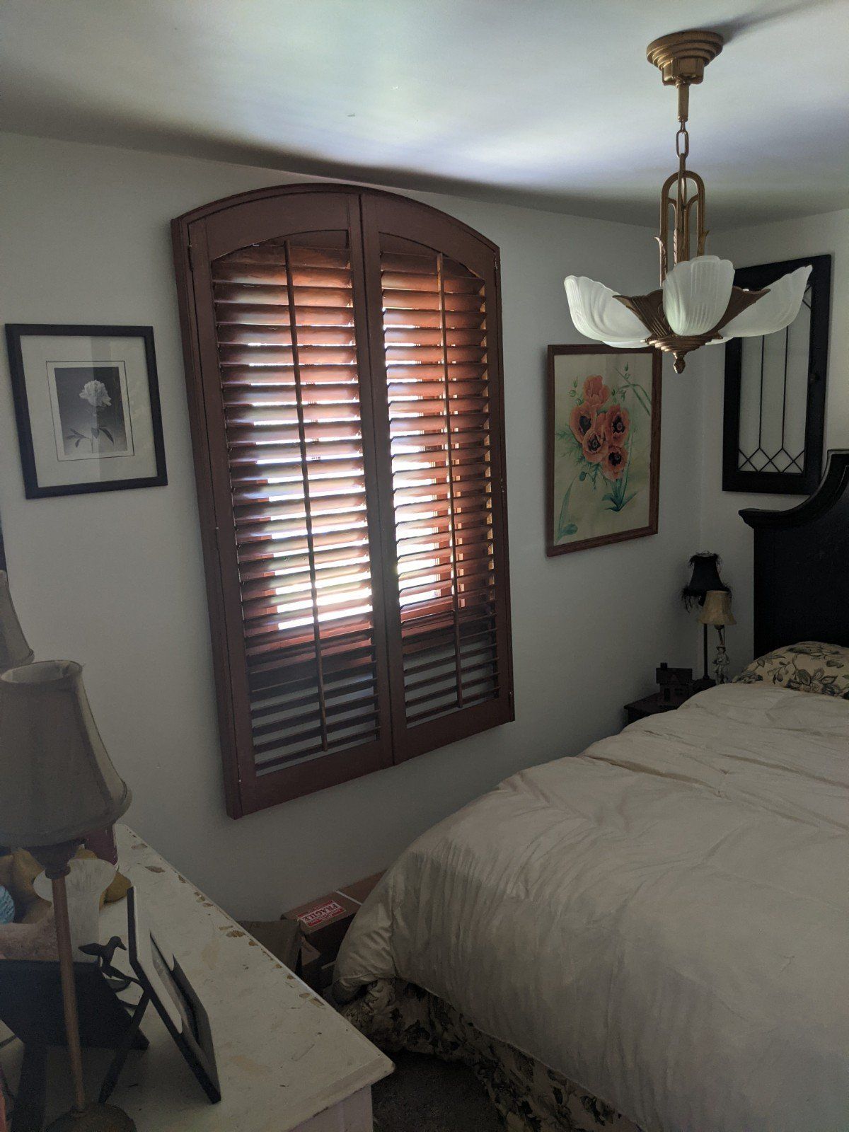 Bedroom with wooden shutters, art, and bed with a floral bedspread.