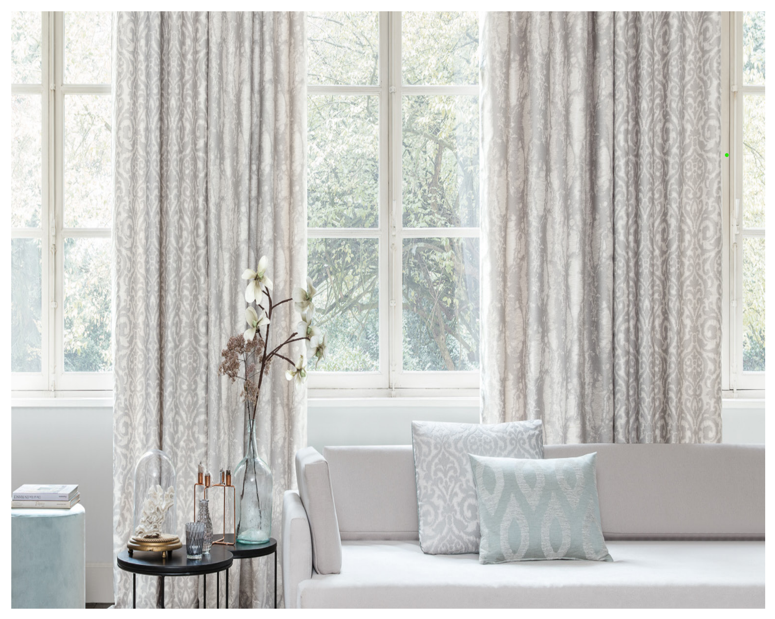 Living room with light gray curtains, white couch, and small table with flowers.