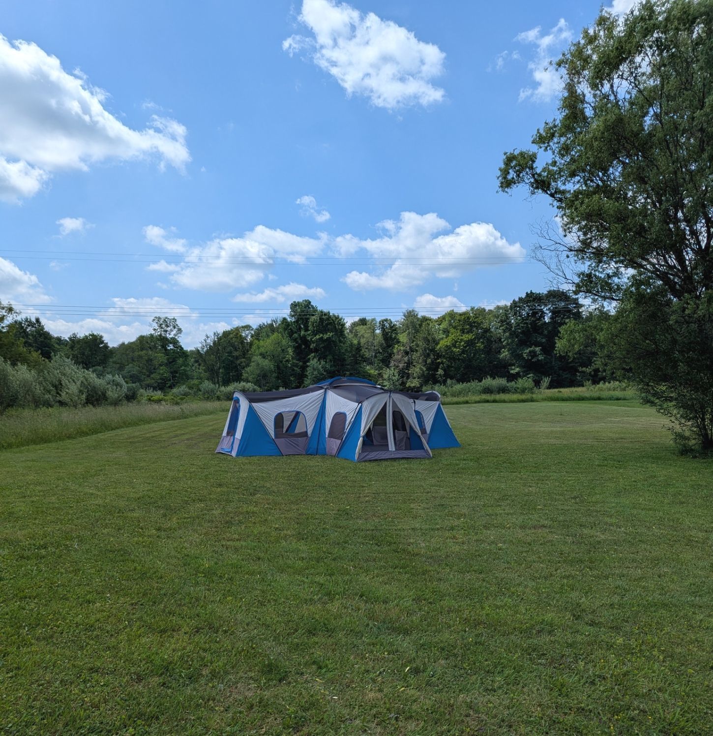 A large blue and gray tent set up on a grassy field under a blue sky.