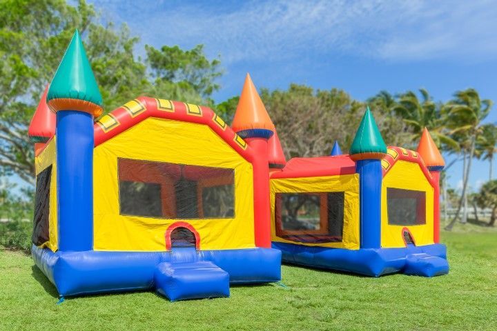 Two colorful inflatable bounce houses on grass in a sunny park