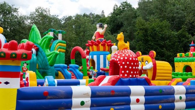 Colorful inflatable bounce park with slides and cartoon-shaped obstacles outdoors under cloudy skies