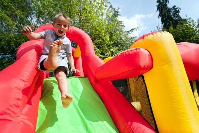 Child sliding down a colorful inflatable slide outdoors, smiling with arms outstretched.