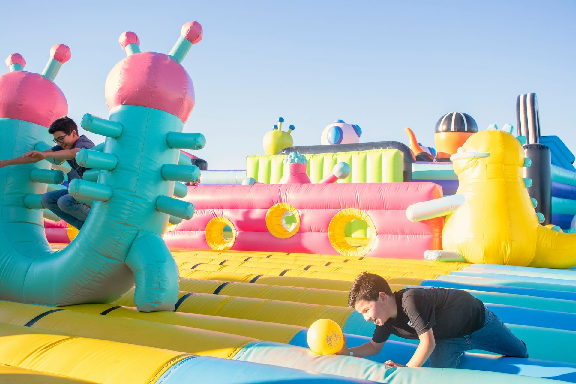 Children playing on colorful inflatable bounce houses at an outdoor fair