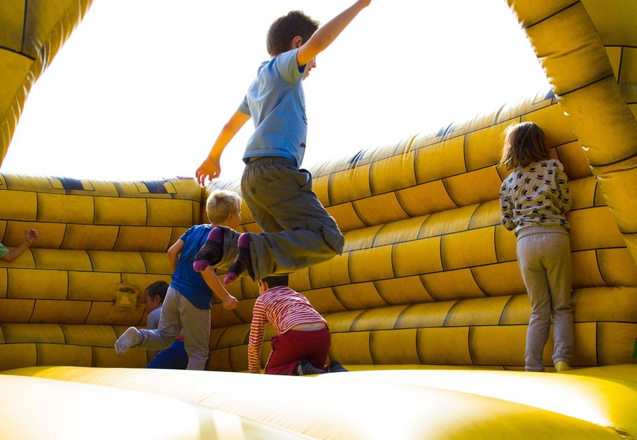 Children climbing on a yellow inflatable bouncy castle, outdoors in bright sunlight
