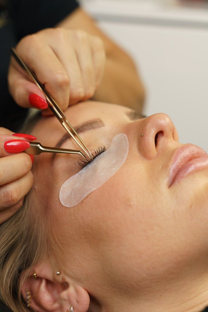 Eine Frau lässt sich Wimpernverlängerungen machen. Die Kosmetikerin appliziert die einzelnen Wimpern mit einer Pinzette
