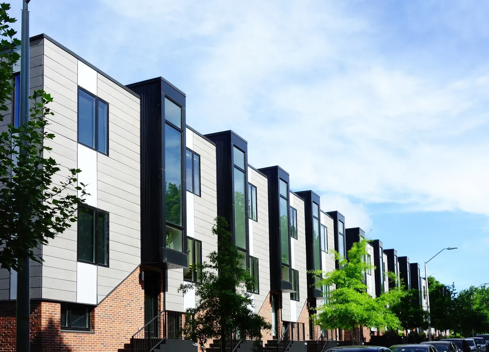 Row of modern townhouses with gray, black, and white exteriors and brick bases under a blue sky.
