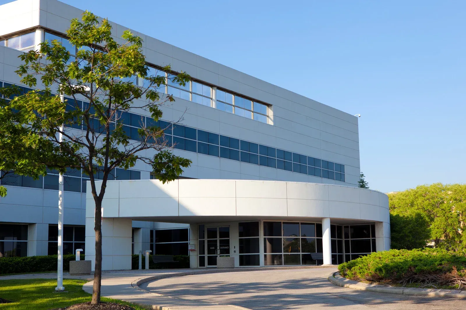 Modern white office building with curved entrance and glass windows under a bright blue sky.