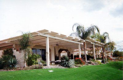 A home with a white pergola, arched doorway, and lush landscaping on a green lawn.