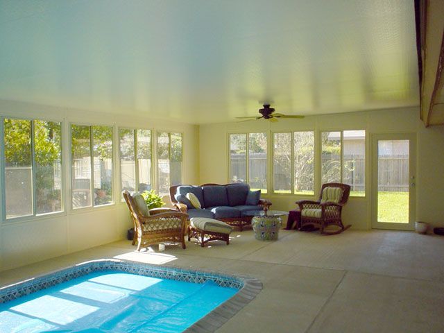 Indoor swimming pool with lounge area, blue sofa, wicker chairs, and large windows.