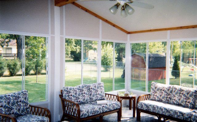 Sunroom with wicker furniture, glass windows, and a view of a backyard.