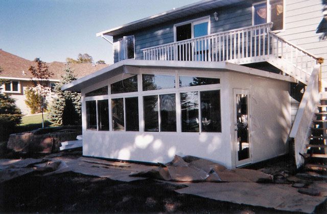 White sunroom addition attached to a two-story house, featuring large windows and an adjacent deck with stairs.