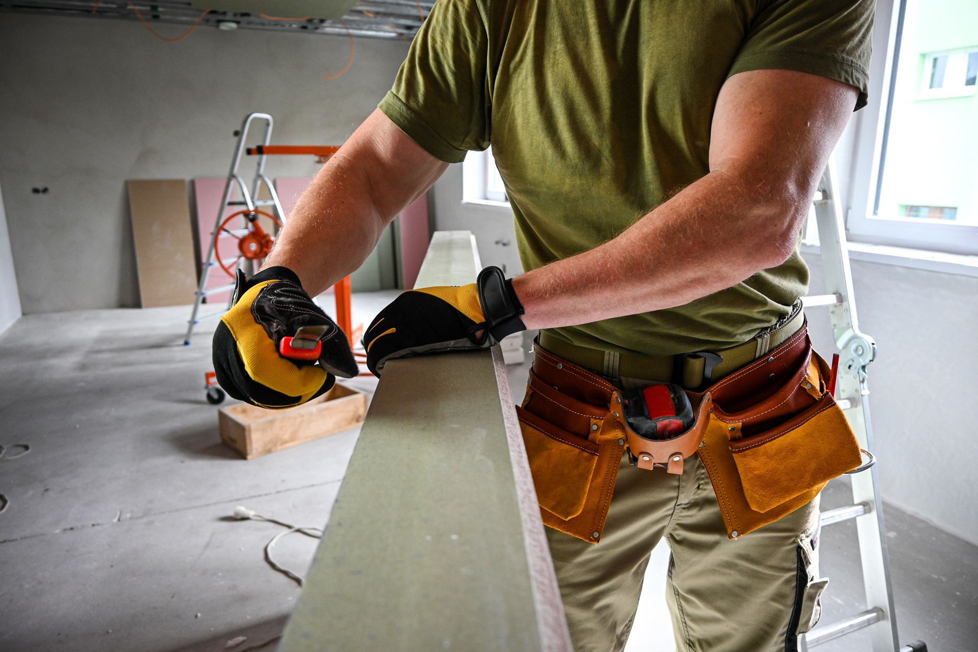 Carpenter wearing gloves, using a sander on a wooden beam, in a construction site.