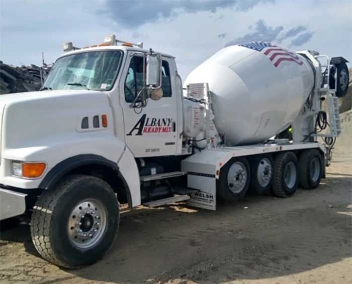 White cement mixer truck with company logo parked on gravel.