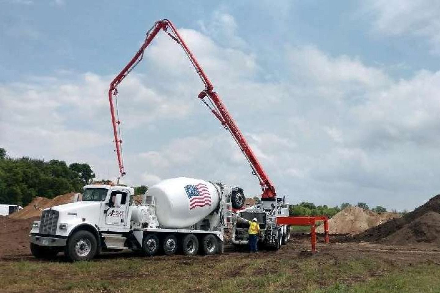Concrete truck with extended boom, pouring concrete on a construction site; blue sky.