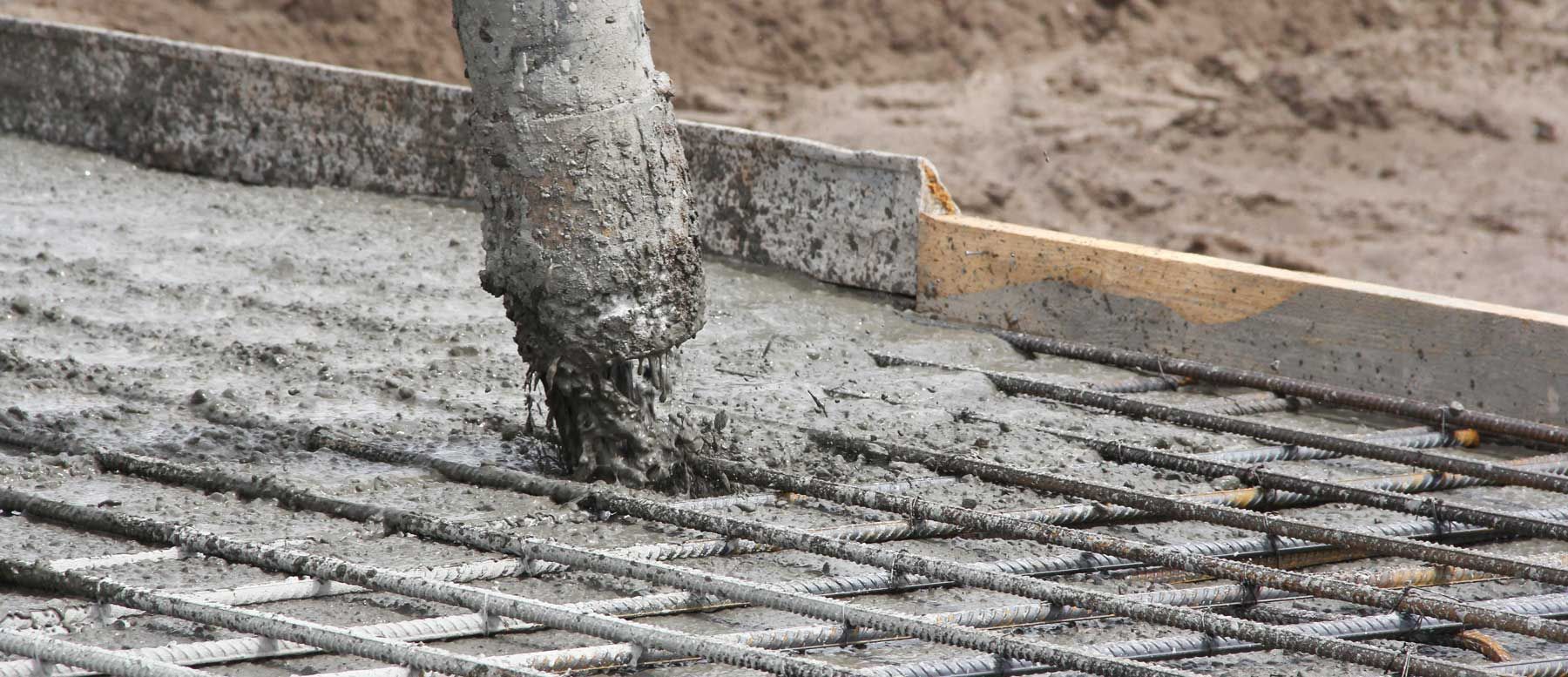 Concrete being poured from a nozzle onto a steel mesh framework.