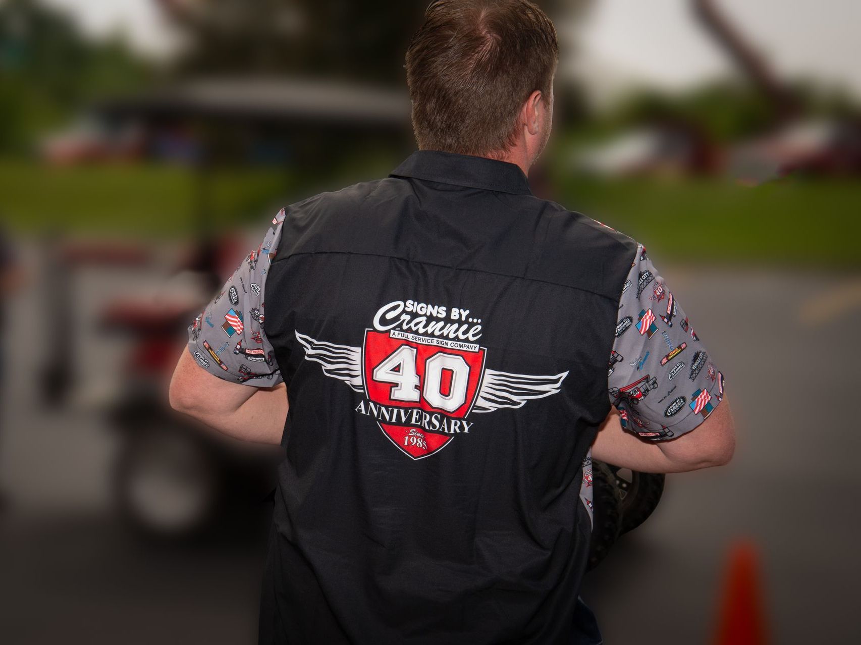 Person seen from behind wearing a black vest with a red-and-white “40” logo at an outdoor event.