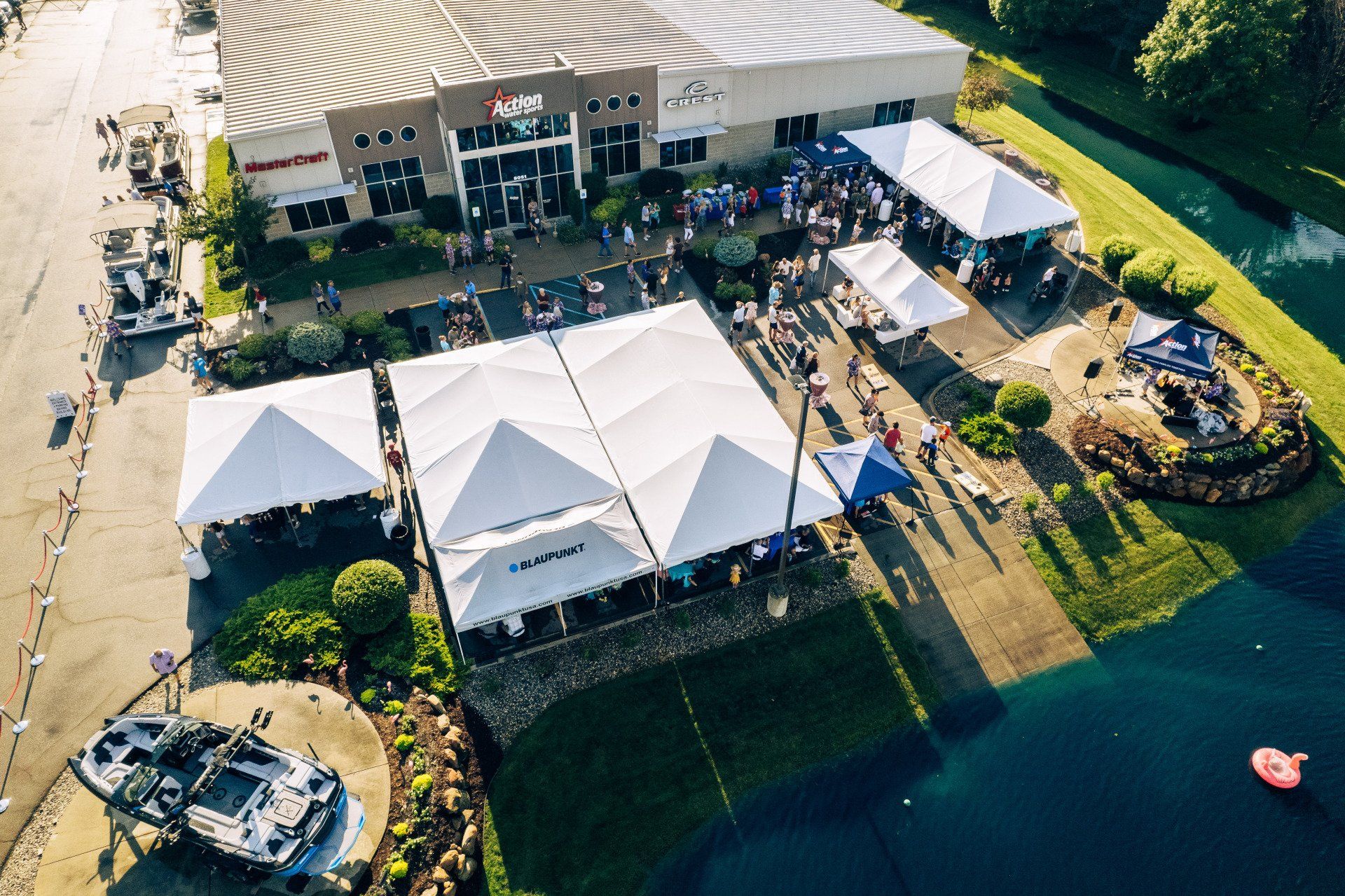 Aerial view of a lakeside event with white tents and a building beside the water