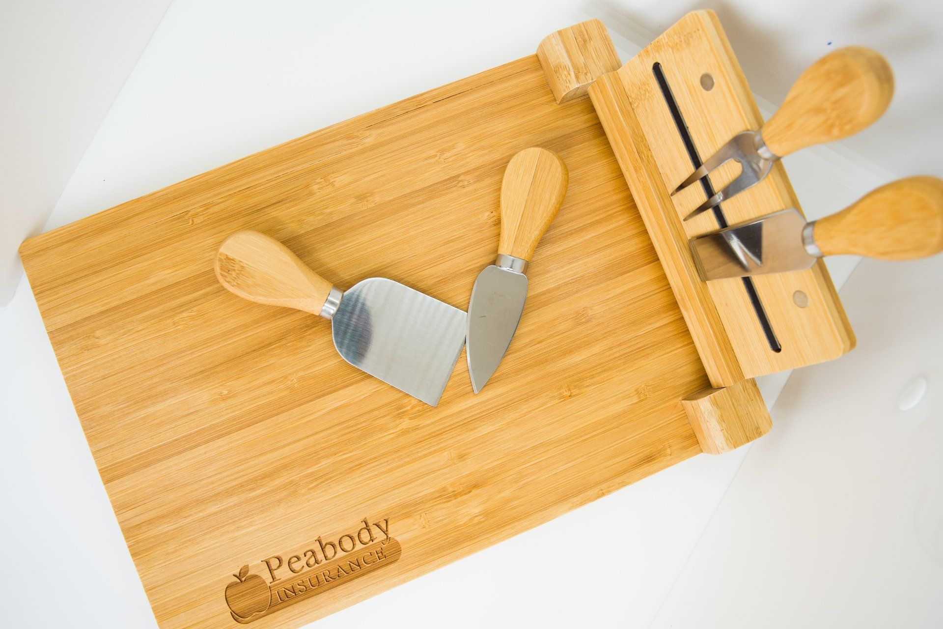 A wooden cutting board with three cheese knives on it.