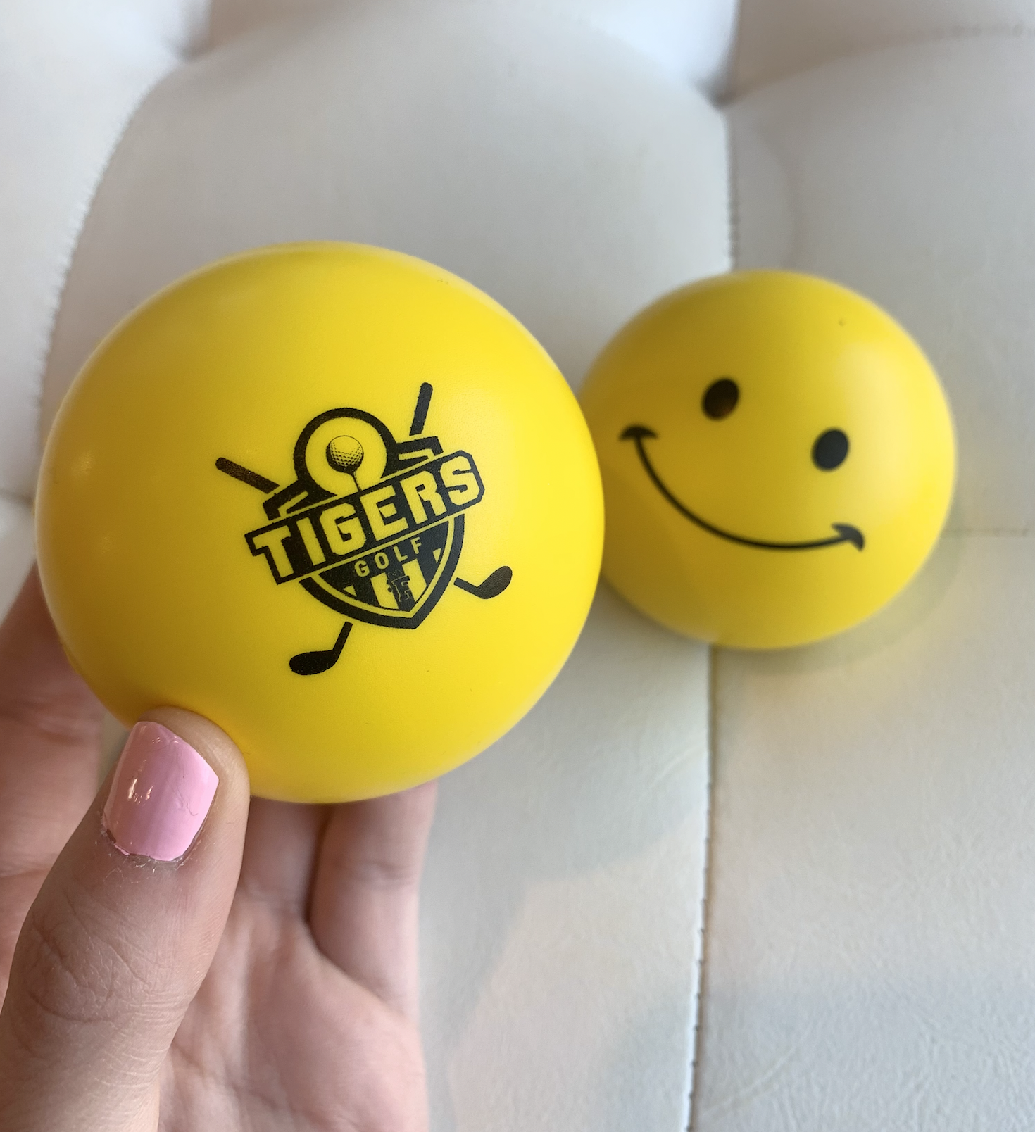 A person is holding a yellow ball that says tigers on it