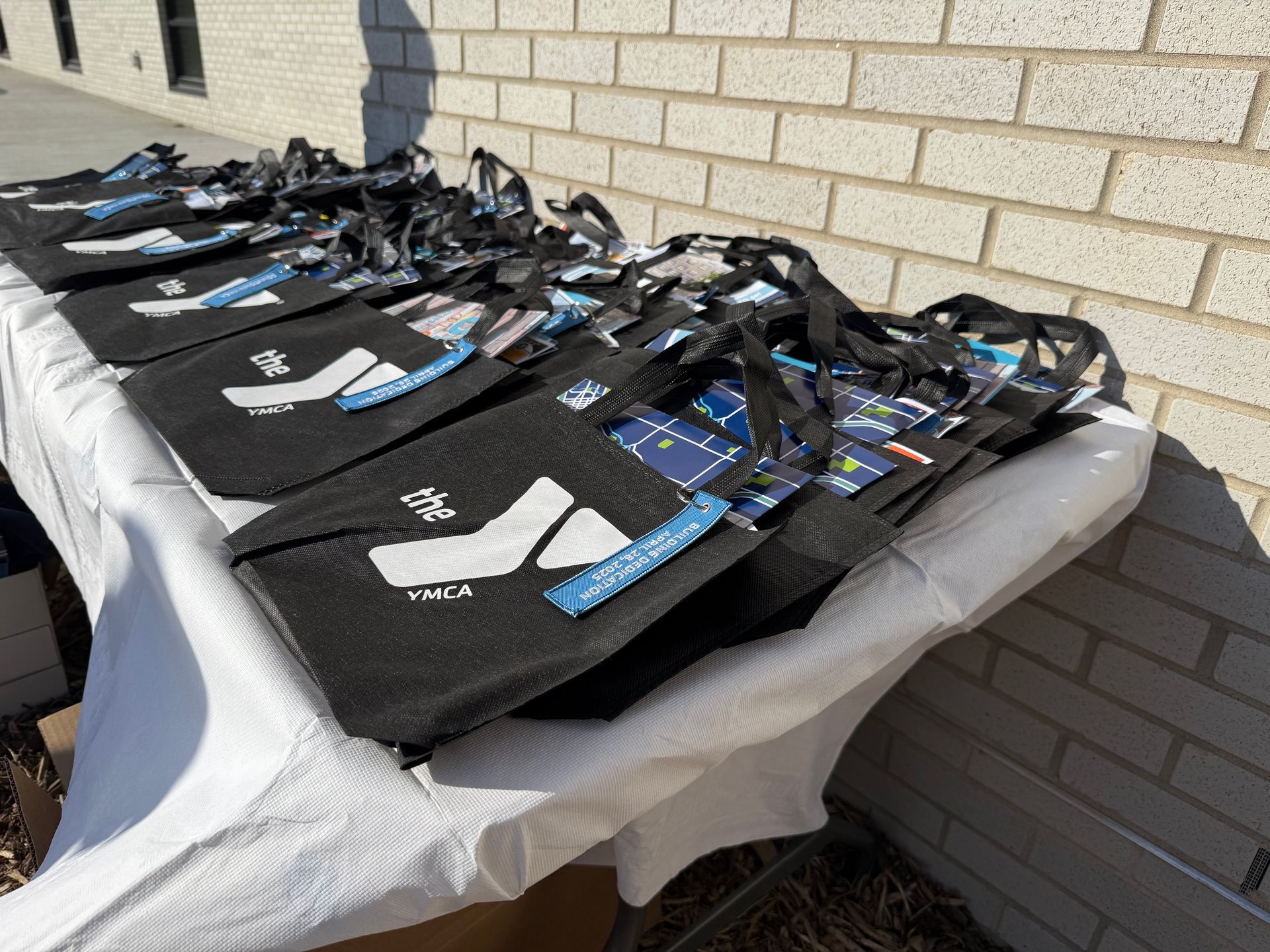 Black bags with blue lanyards laid out on a table against a brick wall.