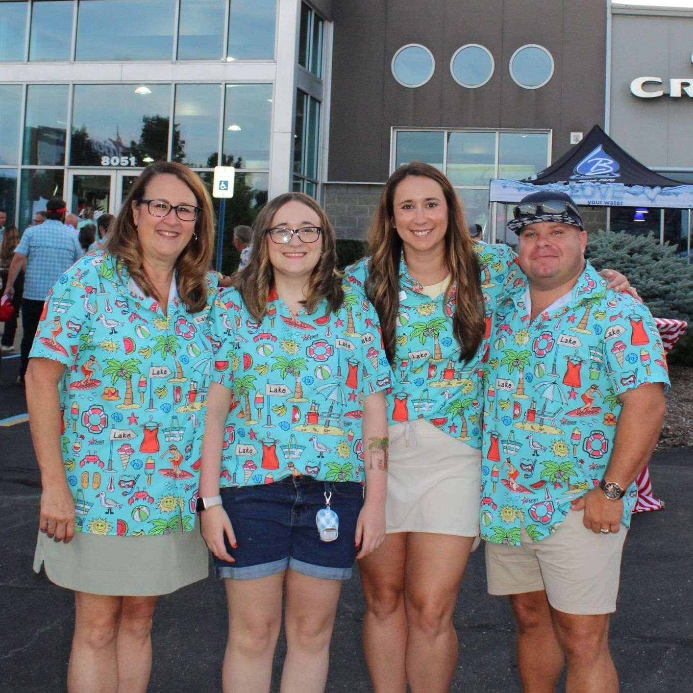 Four people in matching blue Hawaiian shirts standing outside a building, smiling at the camera.