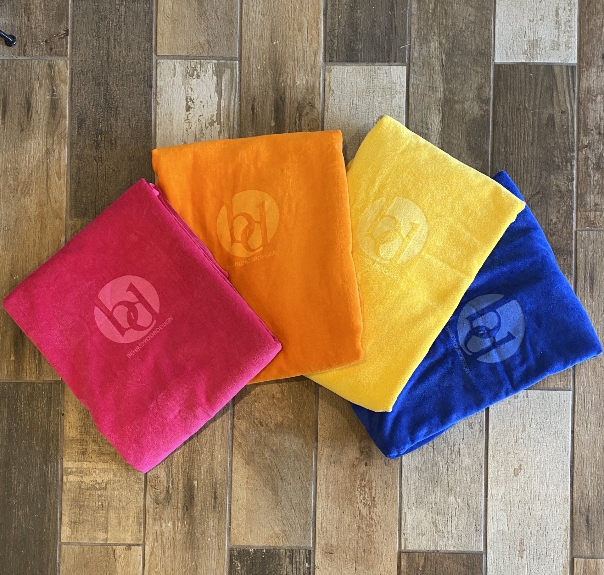 Four colorful towels are stacked on top of each other on a wooden floor