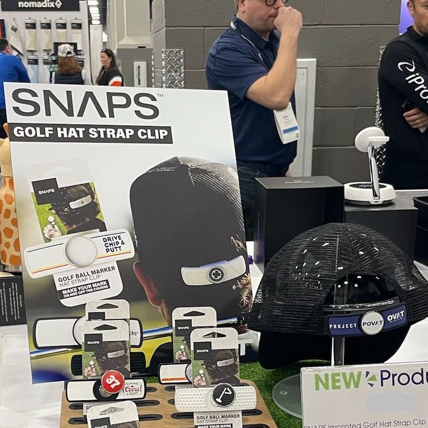 A man stands in front of a sign that says snaps golf hat strap clip