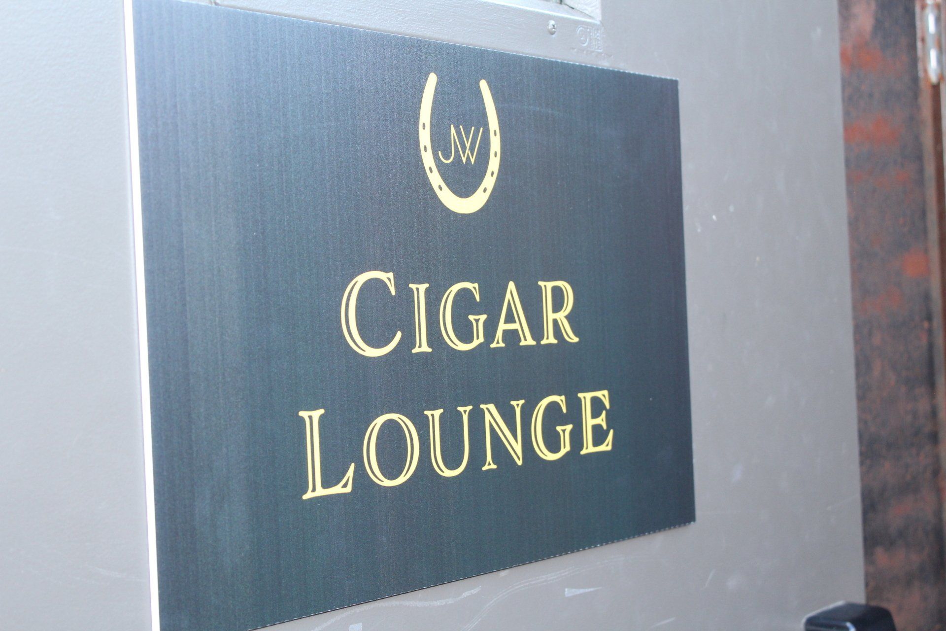 Black sign with gold lettering reading “CIGAR LOUNGE” on a wall.