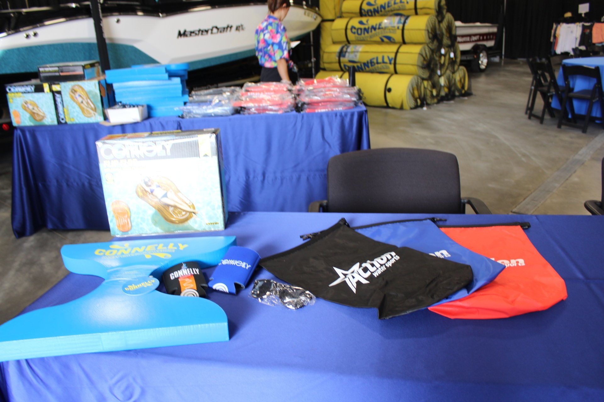 Promotional table with blue tablecloth, T-shirts, and product displays in a warehouse or event space