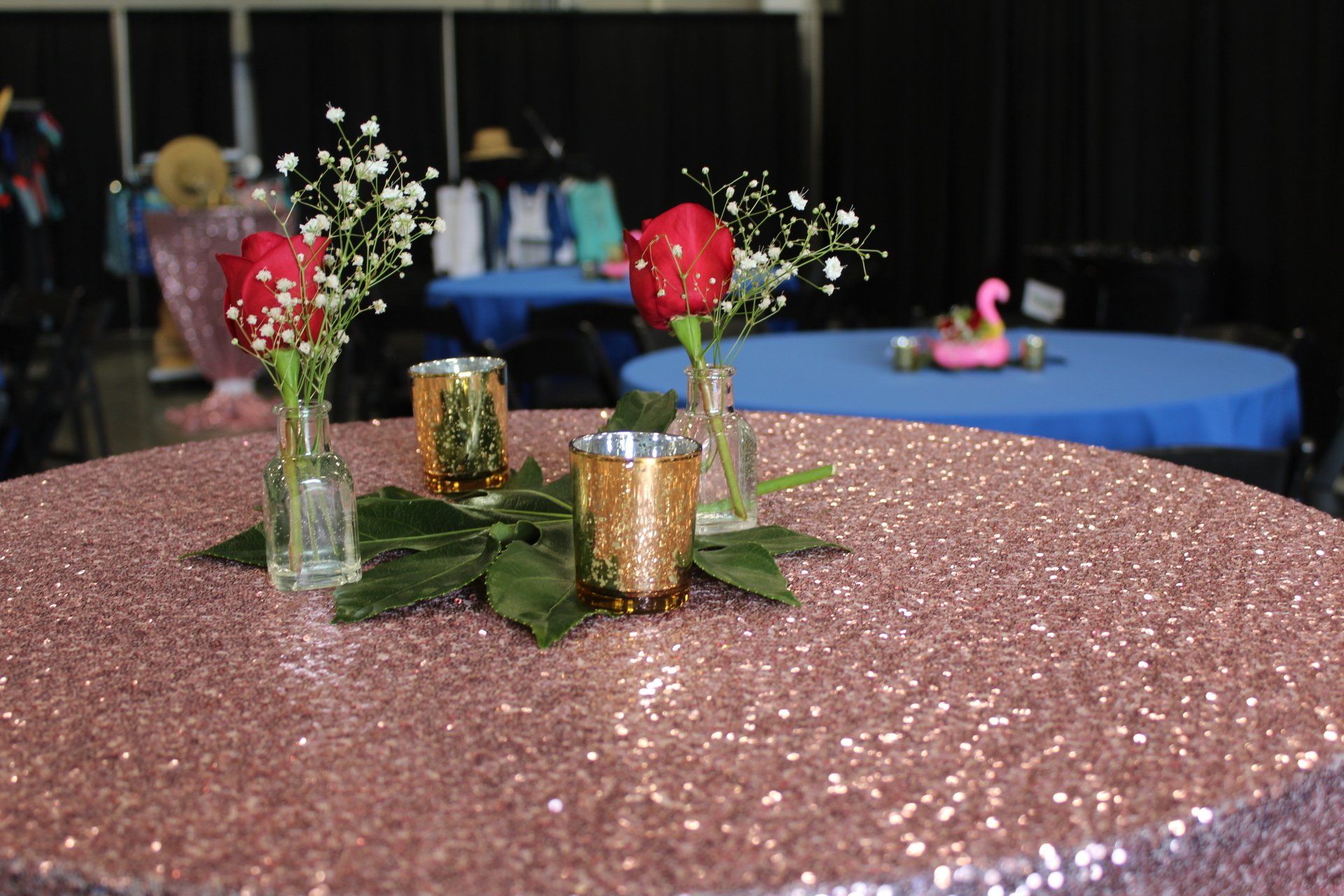 Decorated table with red flowers in glass vases and gold votive candles on a pink glittery tablecloth