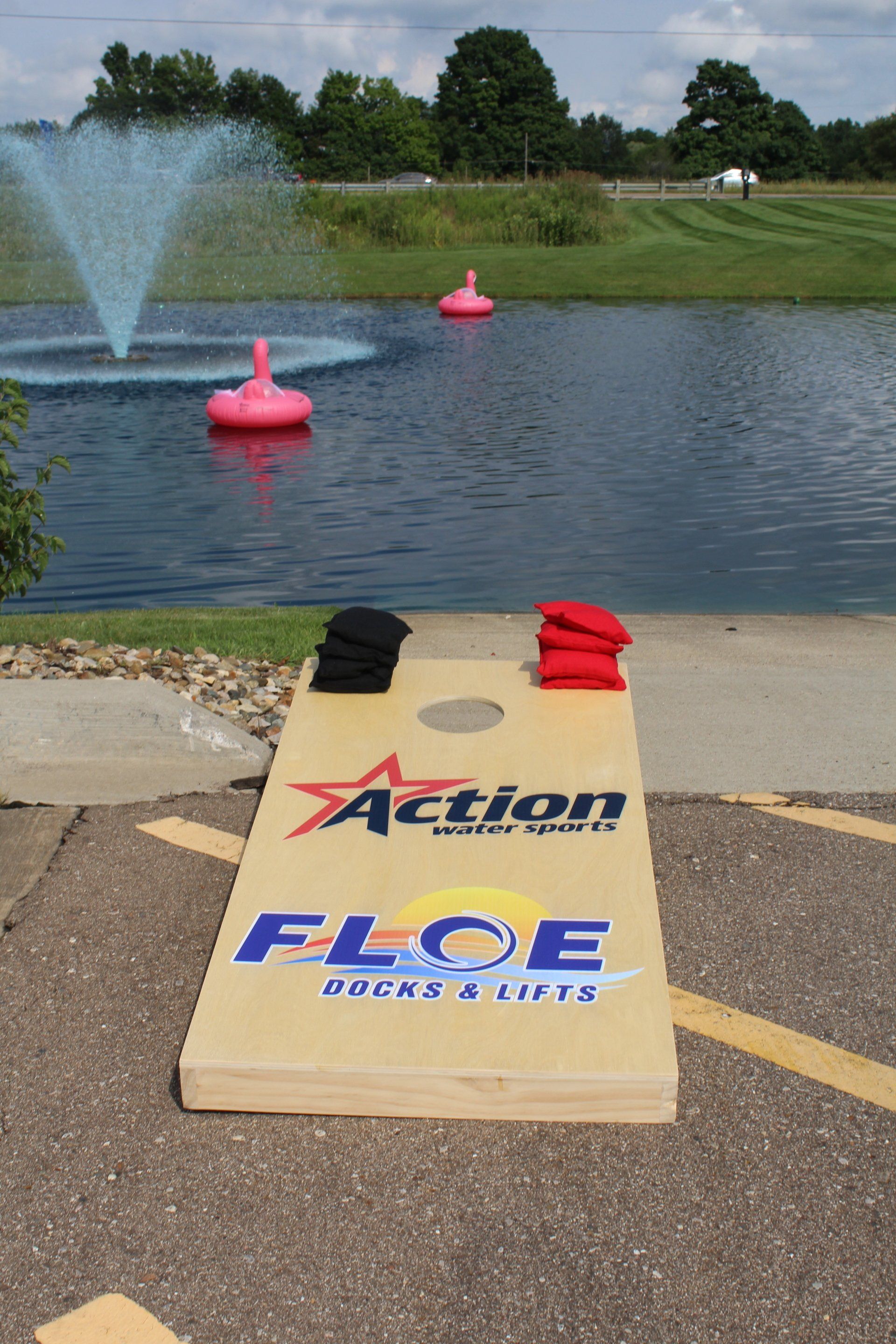 Lake with fountain and pink buoys; foreground has a cardboard sign painted with “Action FLOE” and two hats.