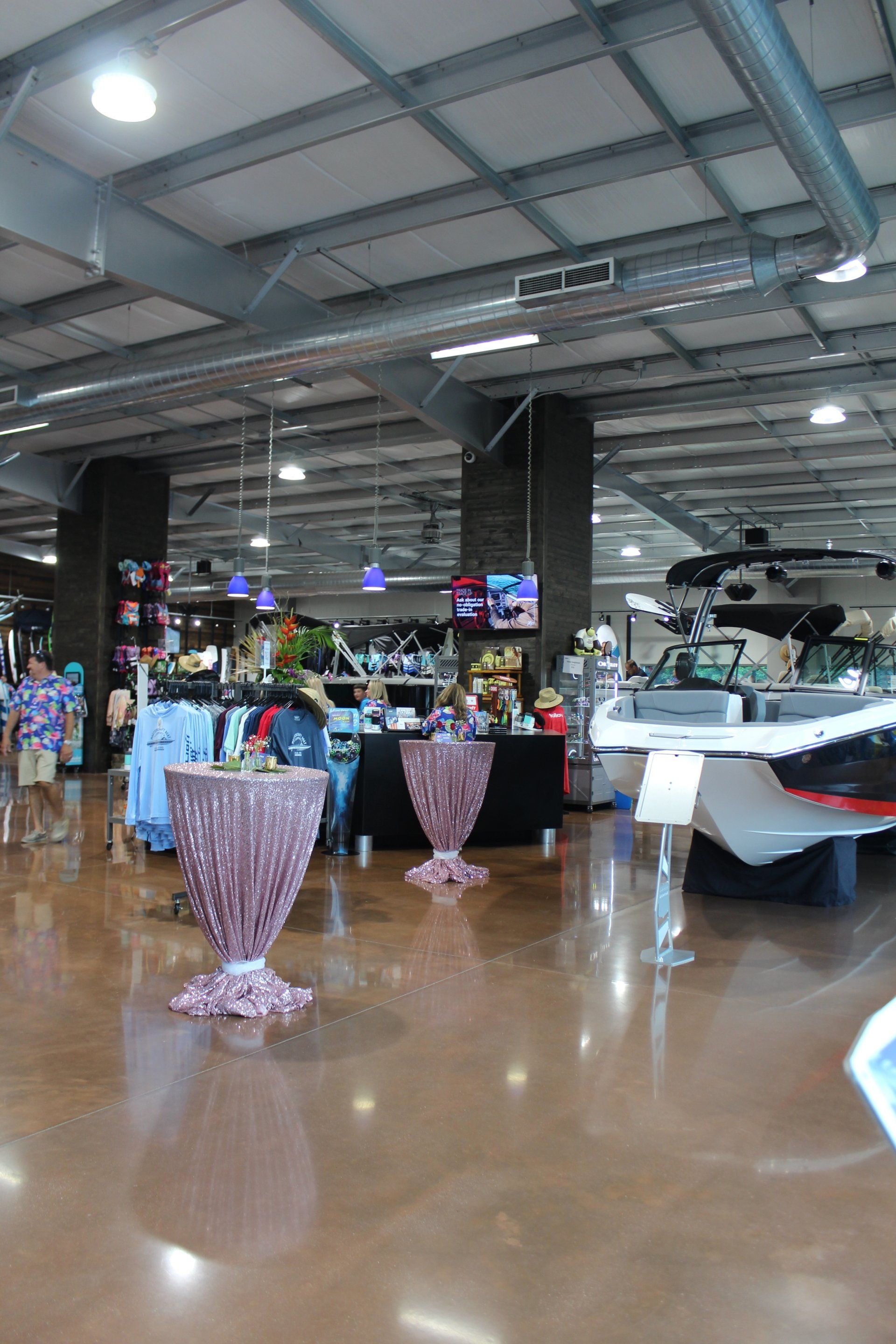 Indoor showroom with boats on display, polished floor, and decorative pink vases under bright industrial lights