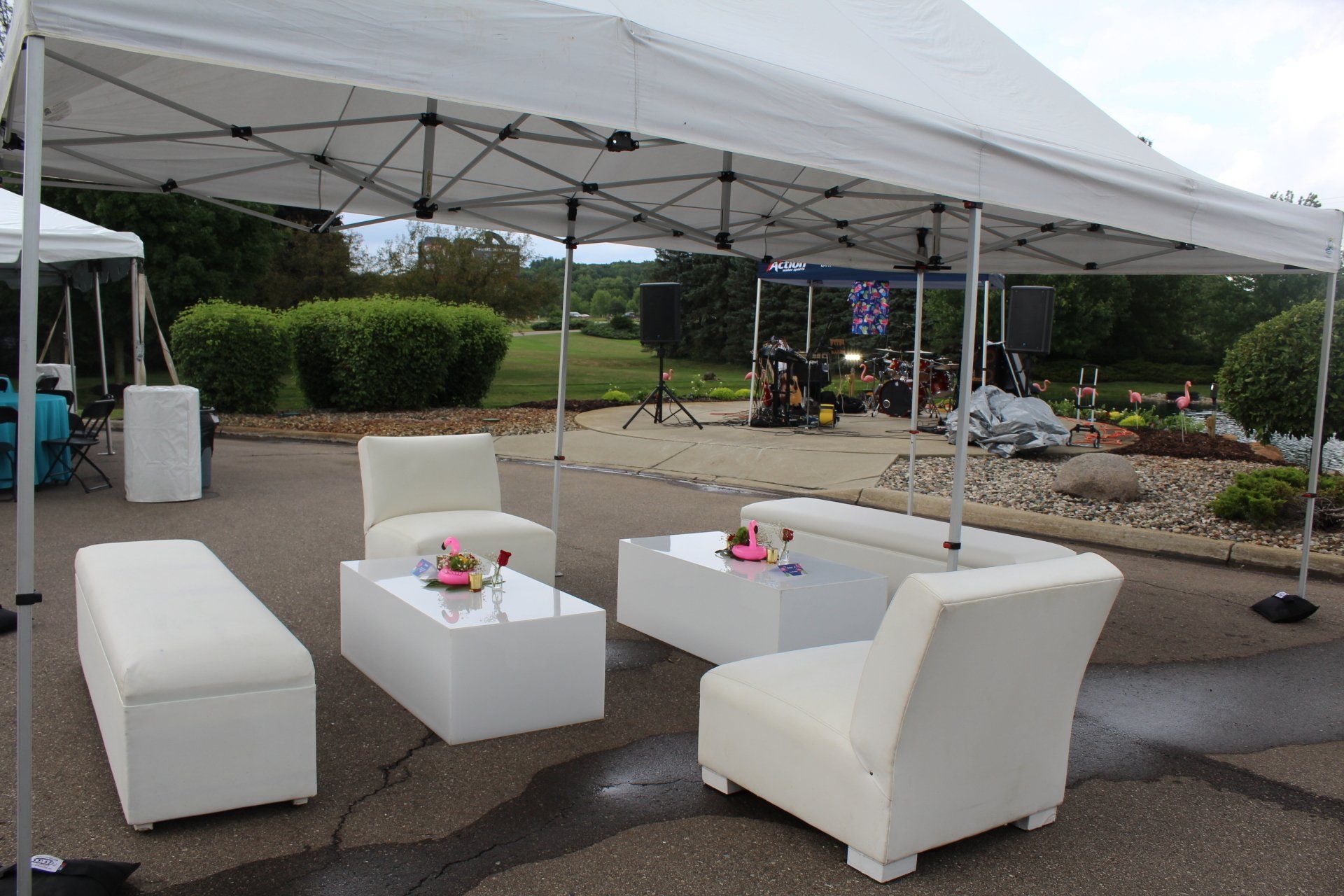 White outdoor seating under a canopy tent on wet pavement, with small tables and a flower display in the background