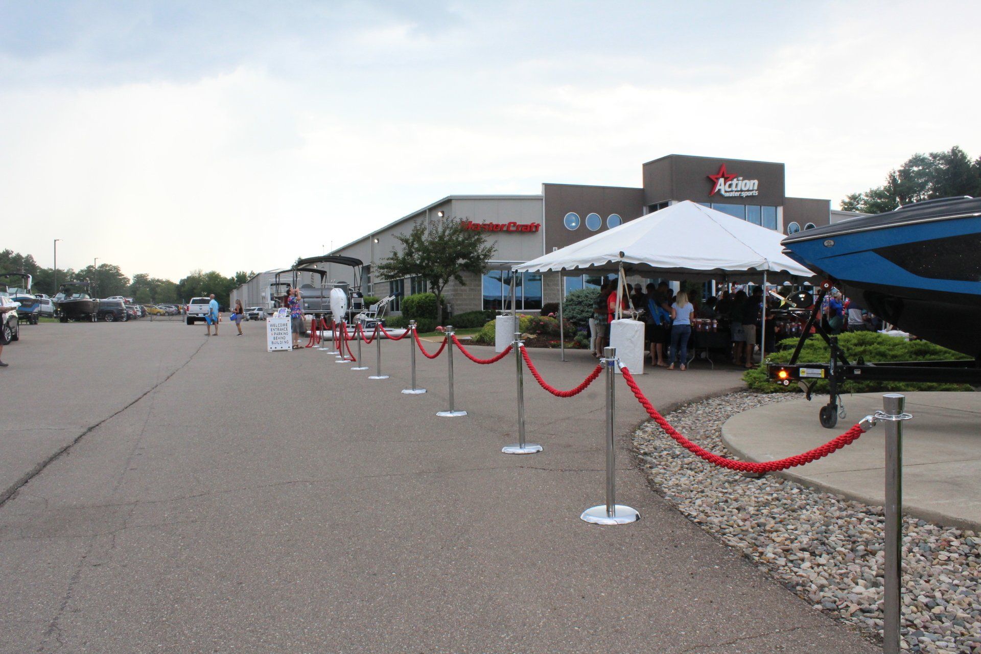 Outdoor store entrance with red velvet ropes, white canopy tent, and people waiting in line.