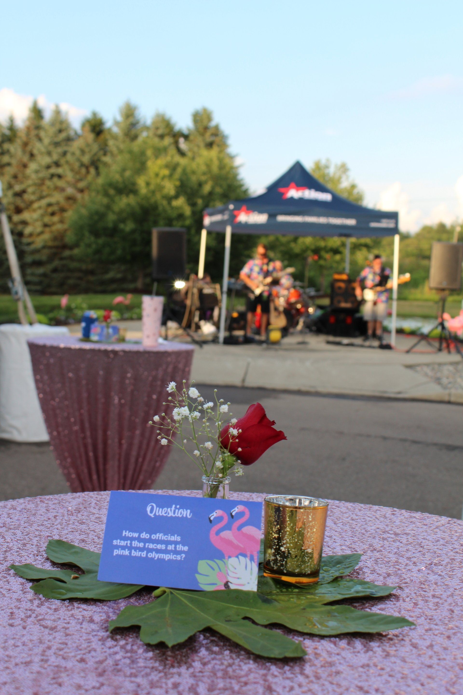 Purple table centerpiece with a blue card and red rose, with a live band playing under a tent in the background