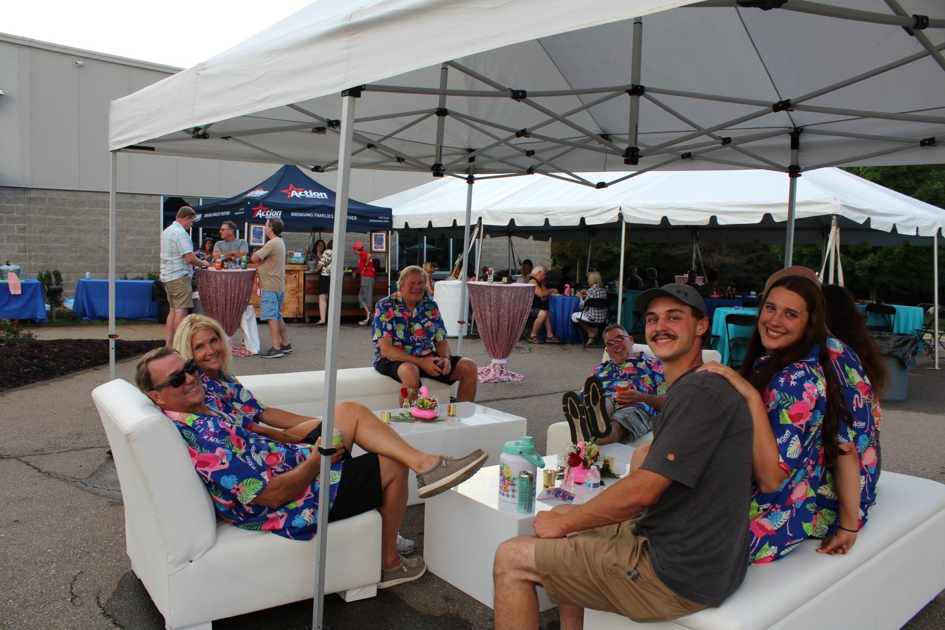 People lounging under a white canopy at an outdoor event, with colorful pillows and tables nearby.