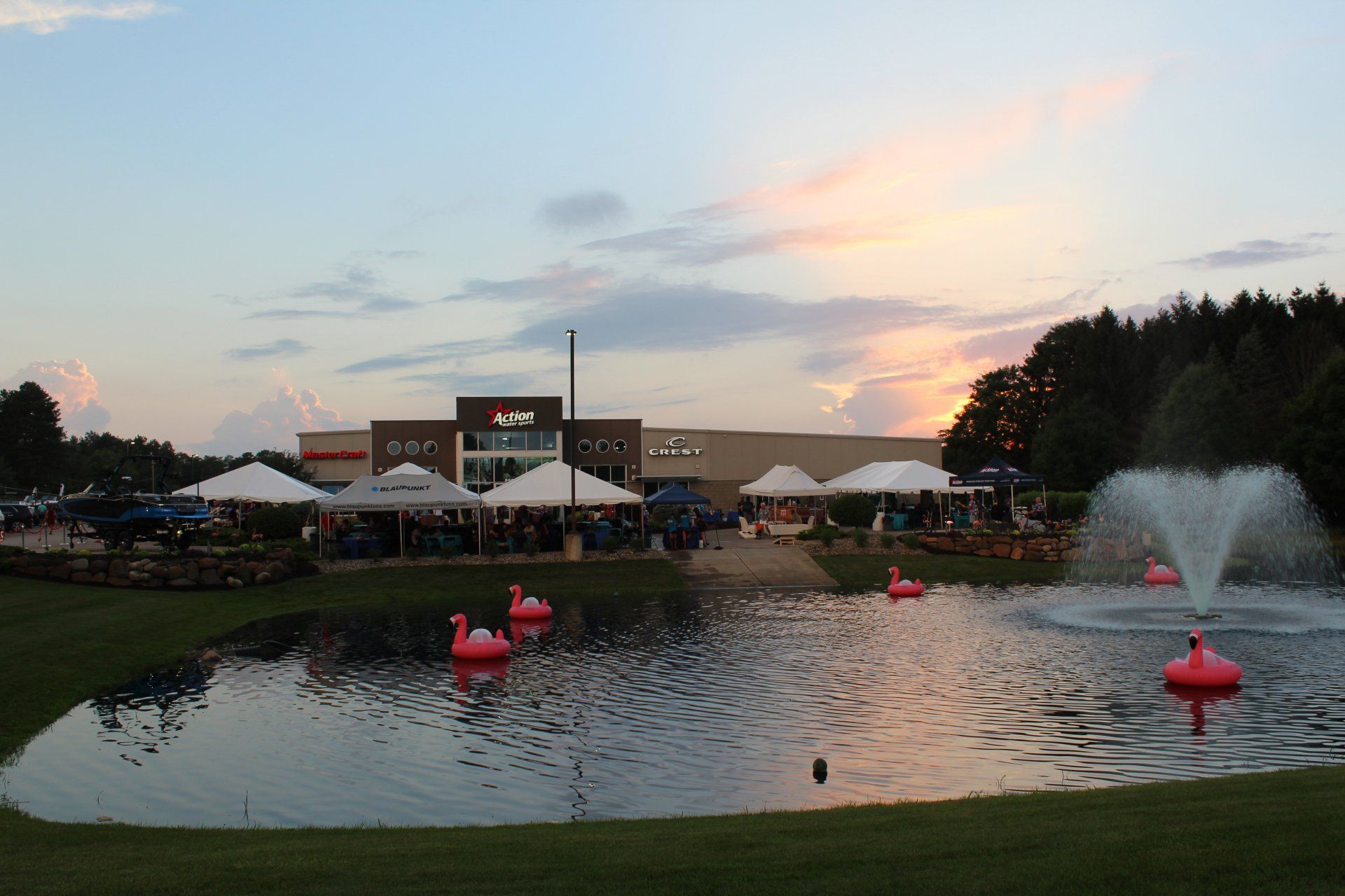 Sunset at a lakeside park with fountain jets, paddle boats, and a building in the background