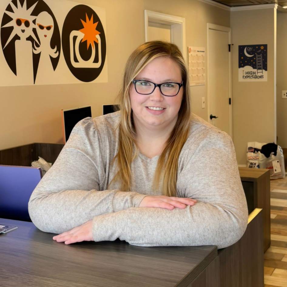 Woman with glasses smiling behind a desk in a bright office lobby