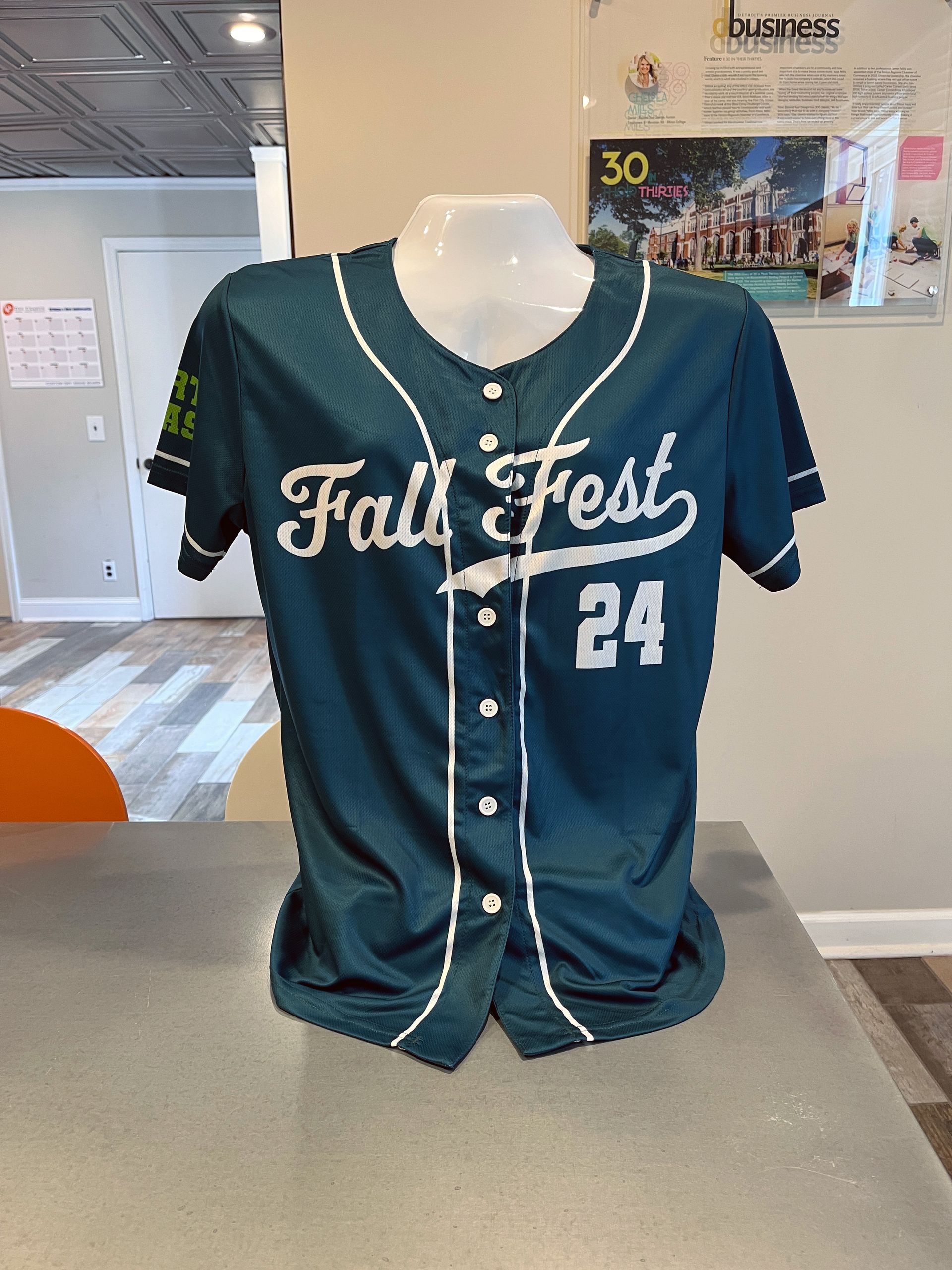 Teal baseball jersey on a mannequin, with white script “Fall Fest” and number 24