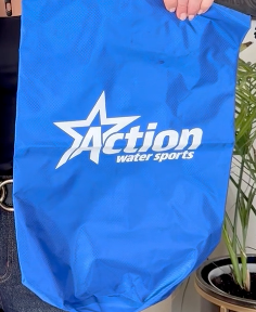 Blue Action Watersports bag with white logo, held up indoors near a plant.