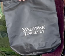 Gray Medawar Jewelers drawstring pouch held outdoors, with green leaves in the background