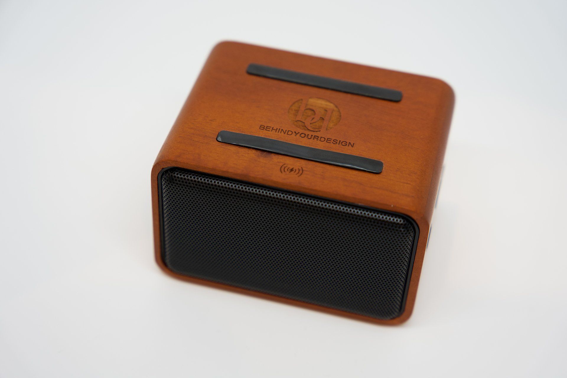 A wooden speaker with a black base is sitting on a white surface.
