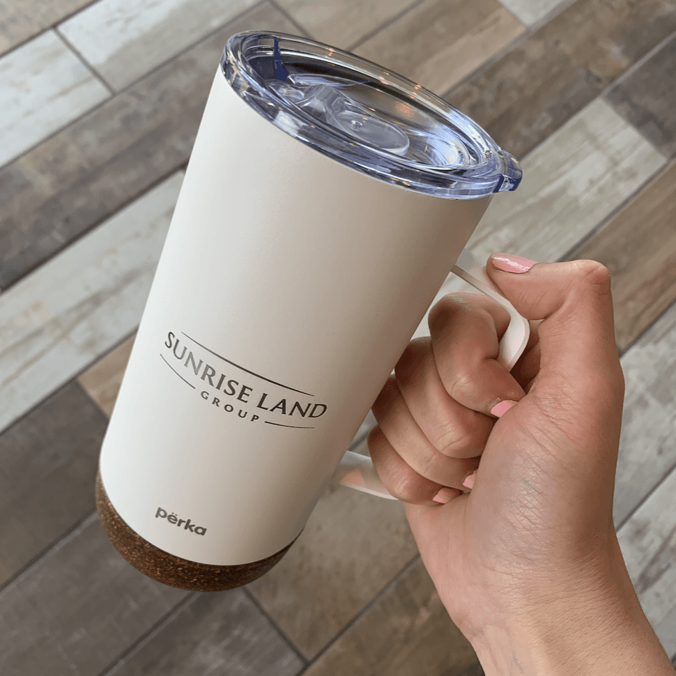 A person is holding a white tumbler that says sunrise land on it