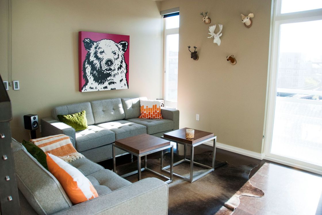 Bright living room with gray sectional, coffee tables, wall art, and sunlight through large windows