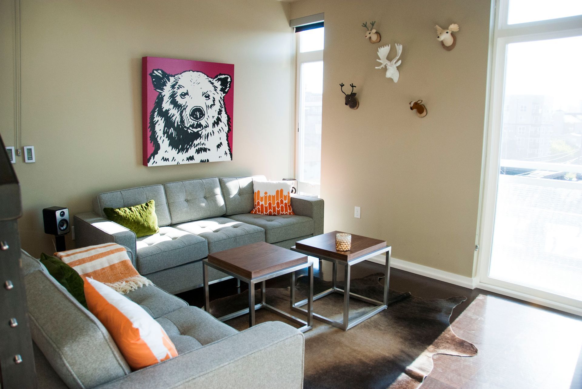 Bright living room with gray sectional, coffee tables, wall art, and sunlight through large windows