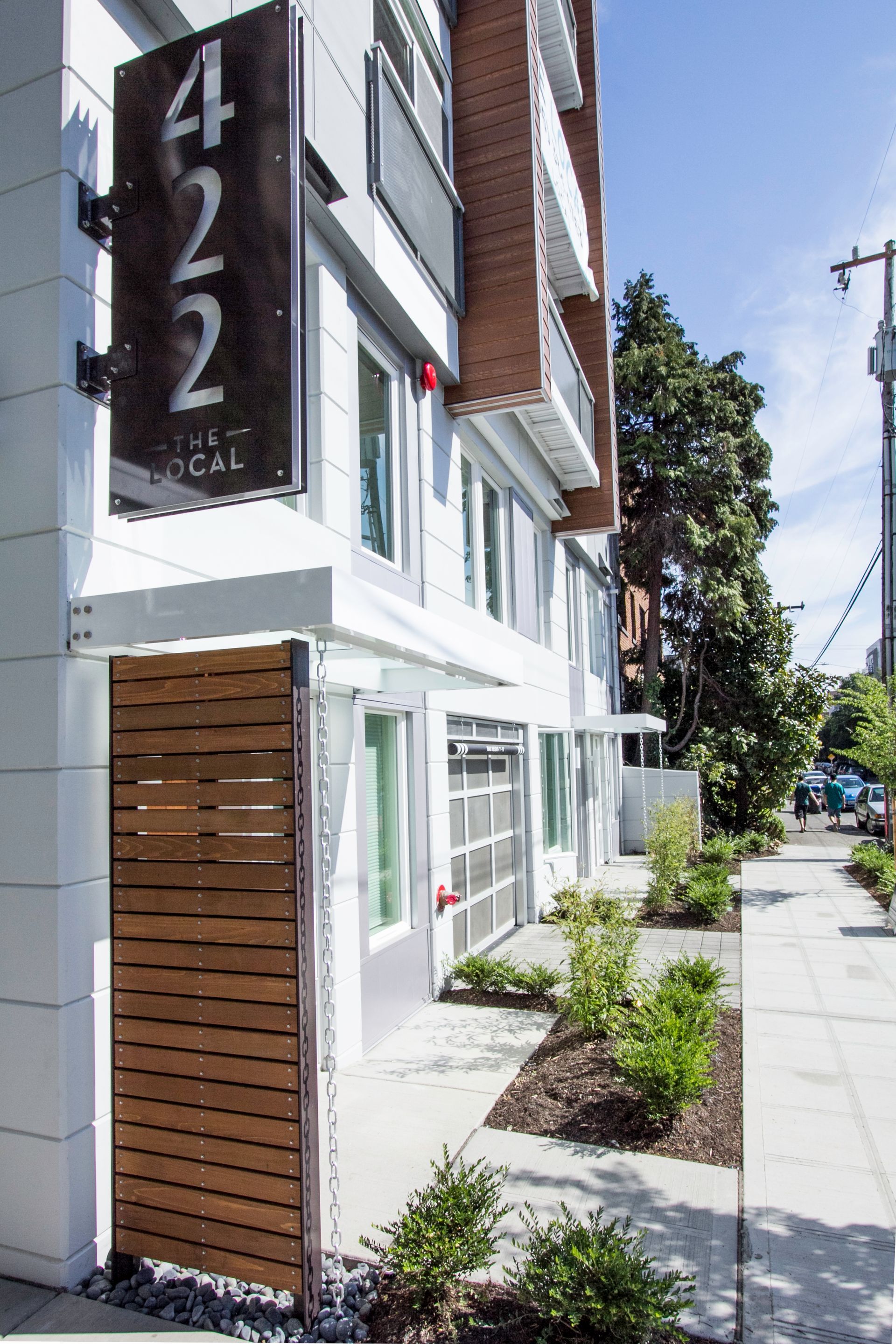 Modern white building with vertical 422 sign, wood paneling, and a sunny sidewalk along the street