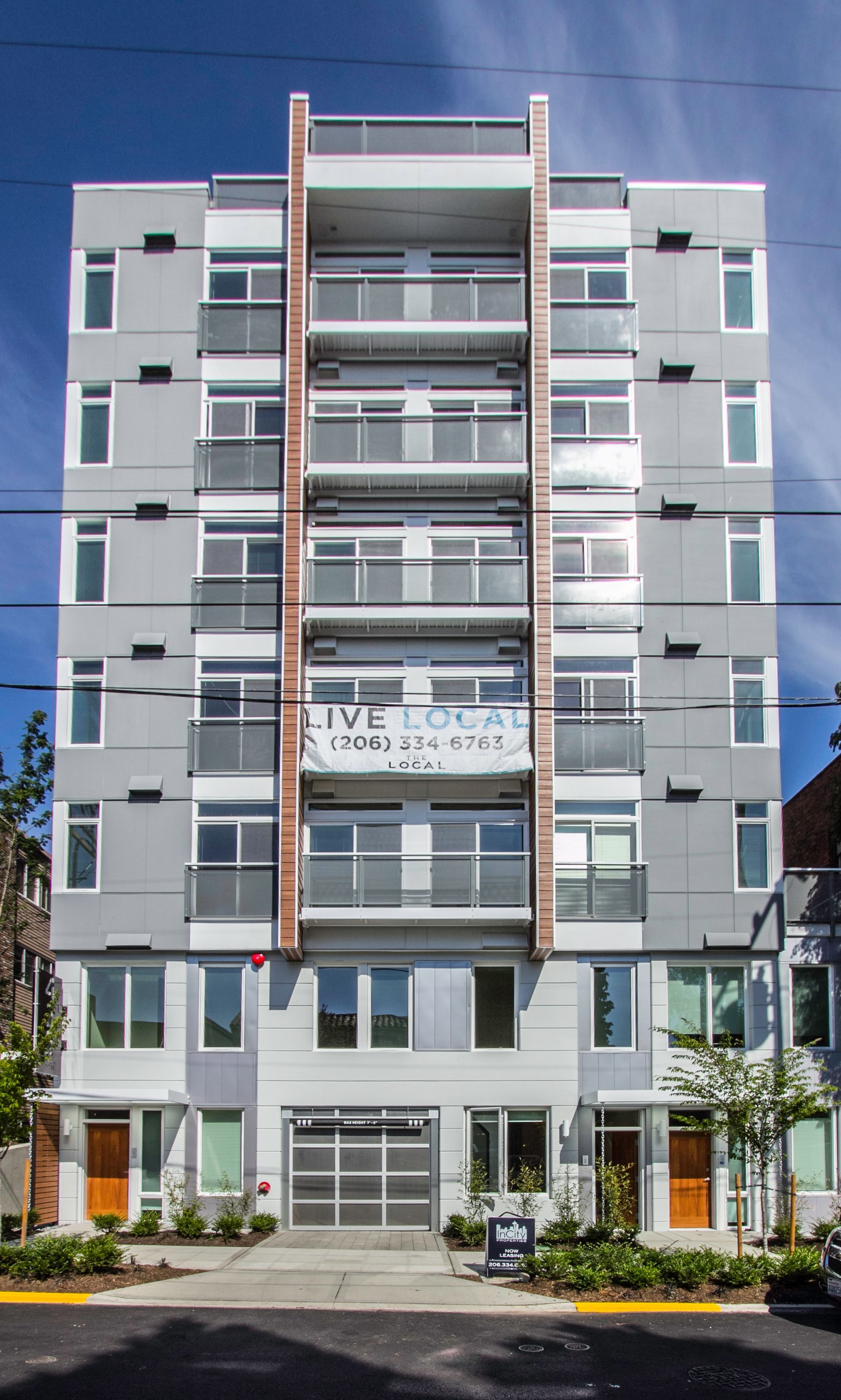 Multi-story gray apartment building with balconies and ground-floor entry on a sunny street