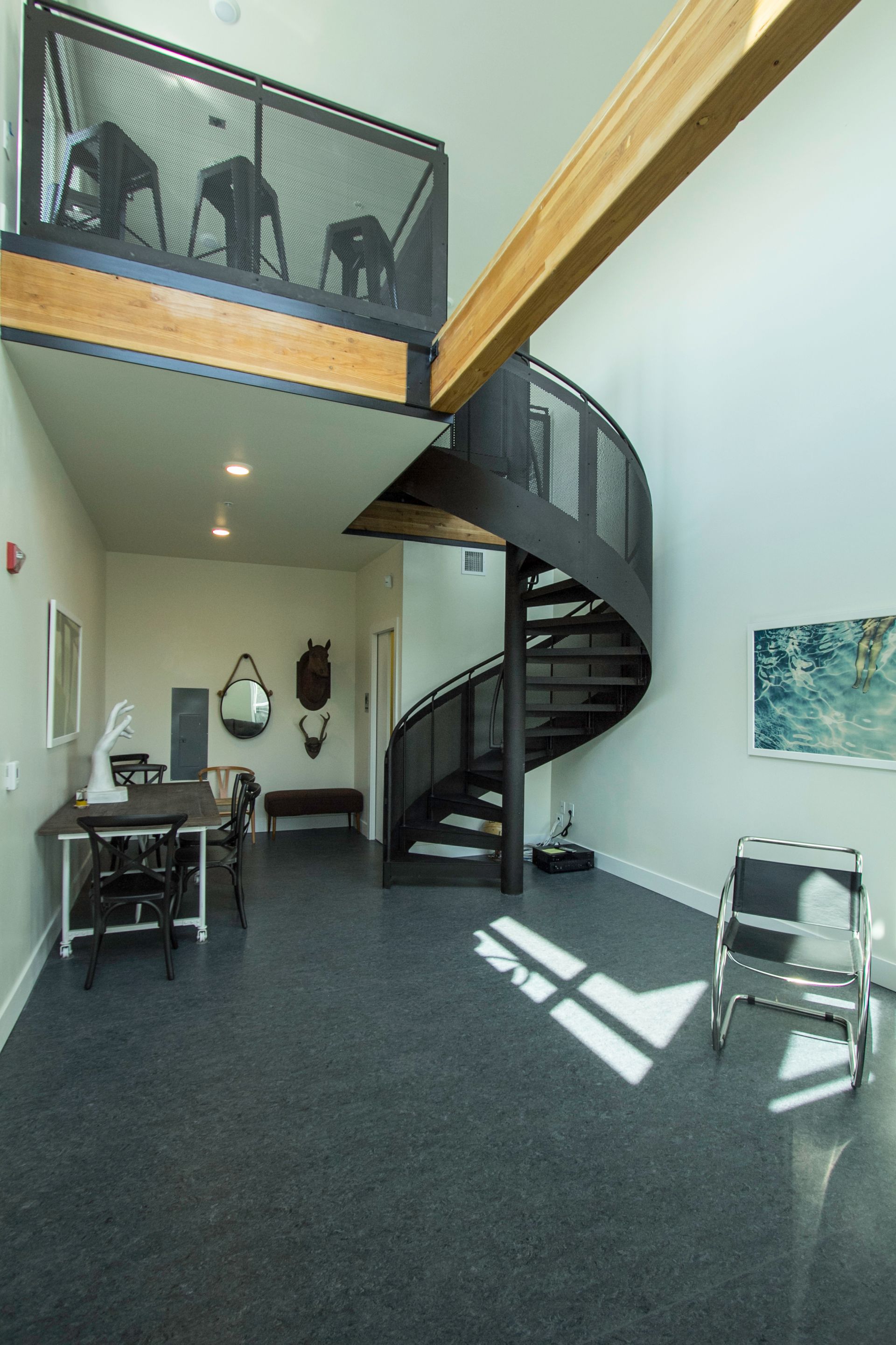 Modern interior with a spiral staircase, balcony railing, desk, and a sunlit white wall