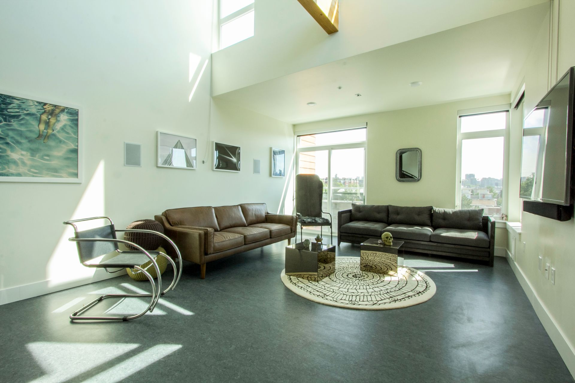 Bright modern living room with brown and black sofas, glass coffee table, and tall windows filling the space with light